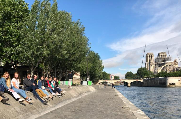 Students sit along the Seine River with Notre Dame in the background