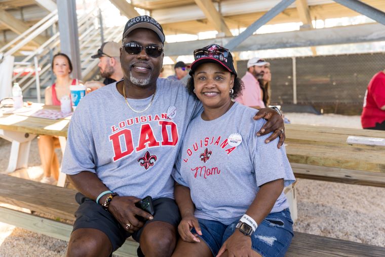 Parents wearing Ragin' Cajun Dad and Ragin' Cajun Mom t-shirts sit in the shade at a Family Weekend event