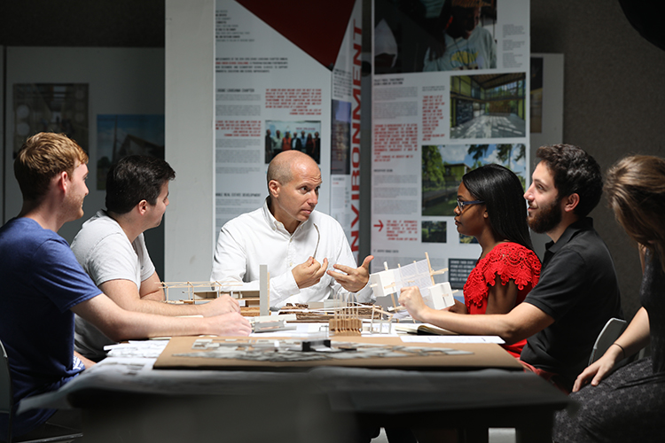 Architecture professor at table discussing structure models with students
