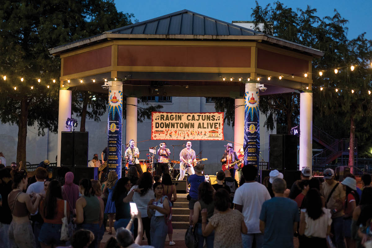A band performs on an outdoor stage with people watching in the foreground.
