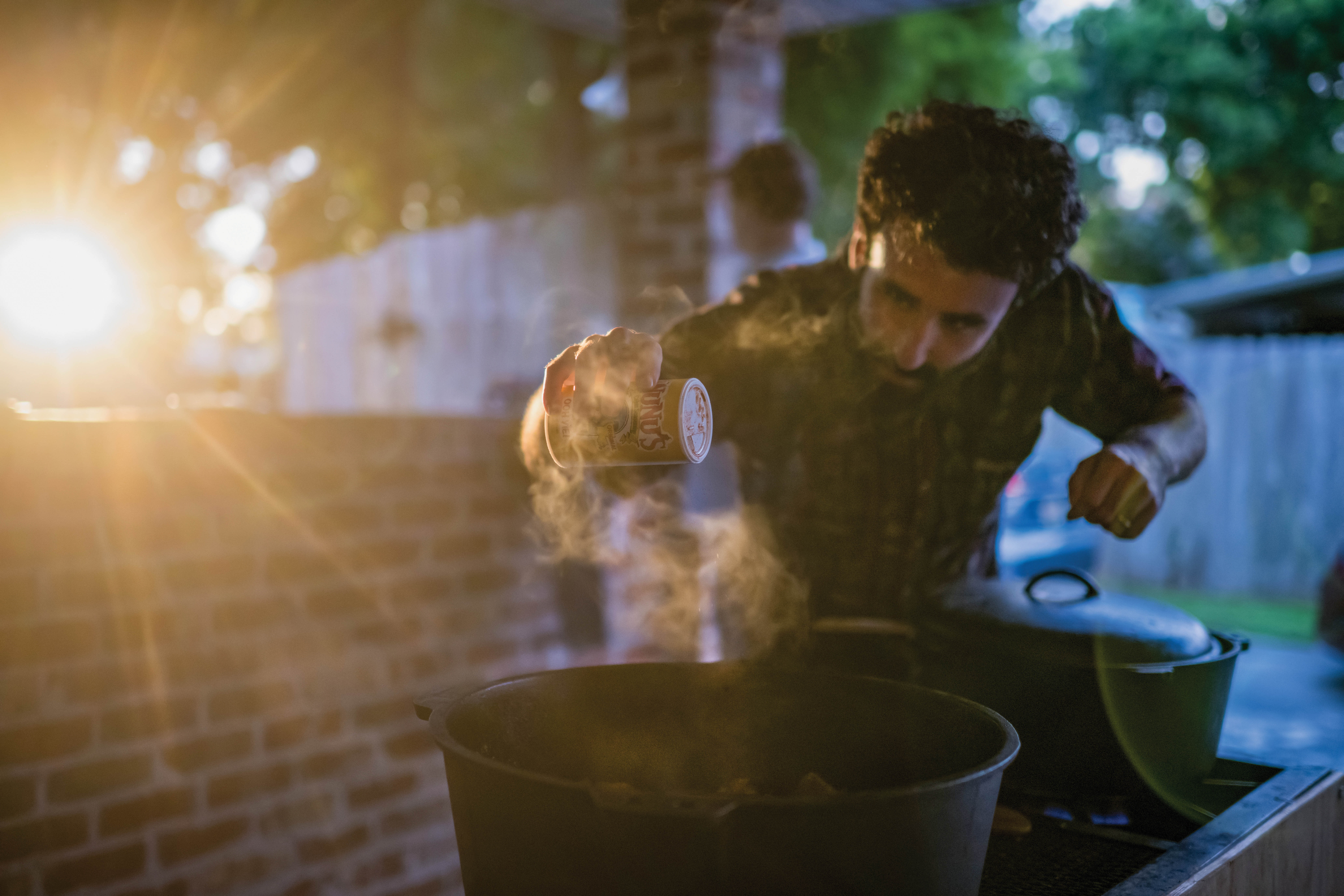 Samuel Frazier pours Cajun seasoning into a black cast iron pot on an outdoor grill..