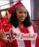 Graduate of the online kinesiology degree program smiles in a cap and gown, holding a sign that reads: 'I finished!' 