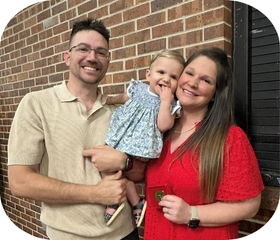 Graduate of the MEd in Educational Leadership smiles with husband and child holding a UL Lafayette pin.