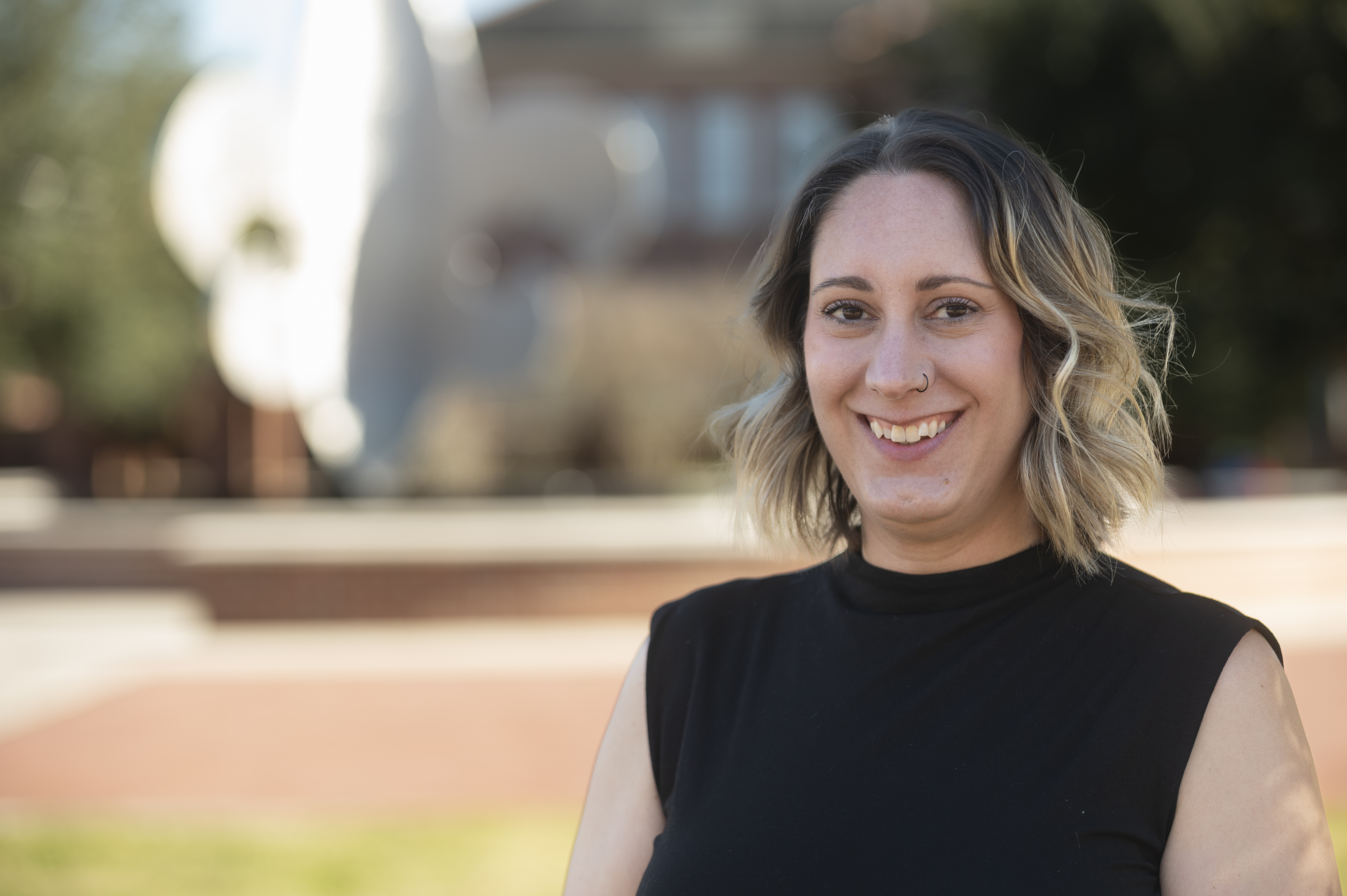 Lindsey Croall wears a black blouse as she stands in front of the fleur de lis fountain in the quad at UL Lafayette.