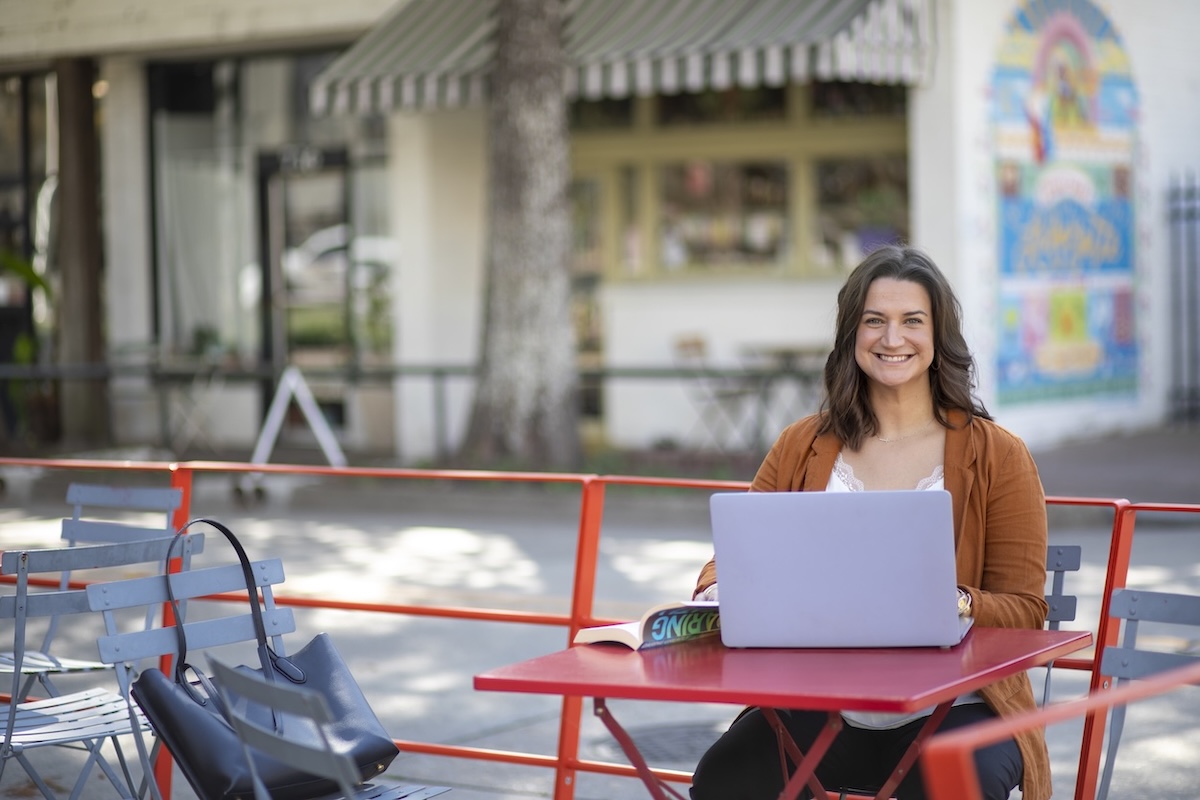 JoElle Judice sits at an outdoor table with a laptop in downtown Lafayette.