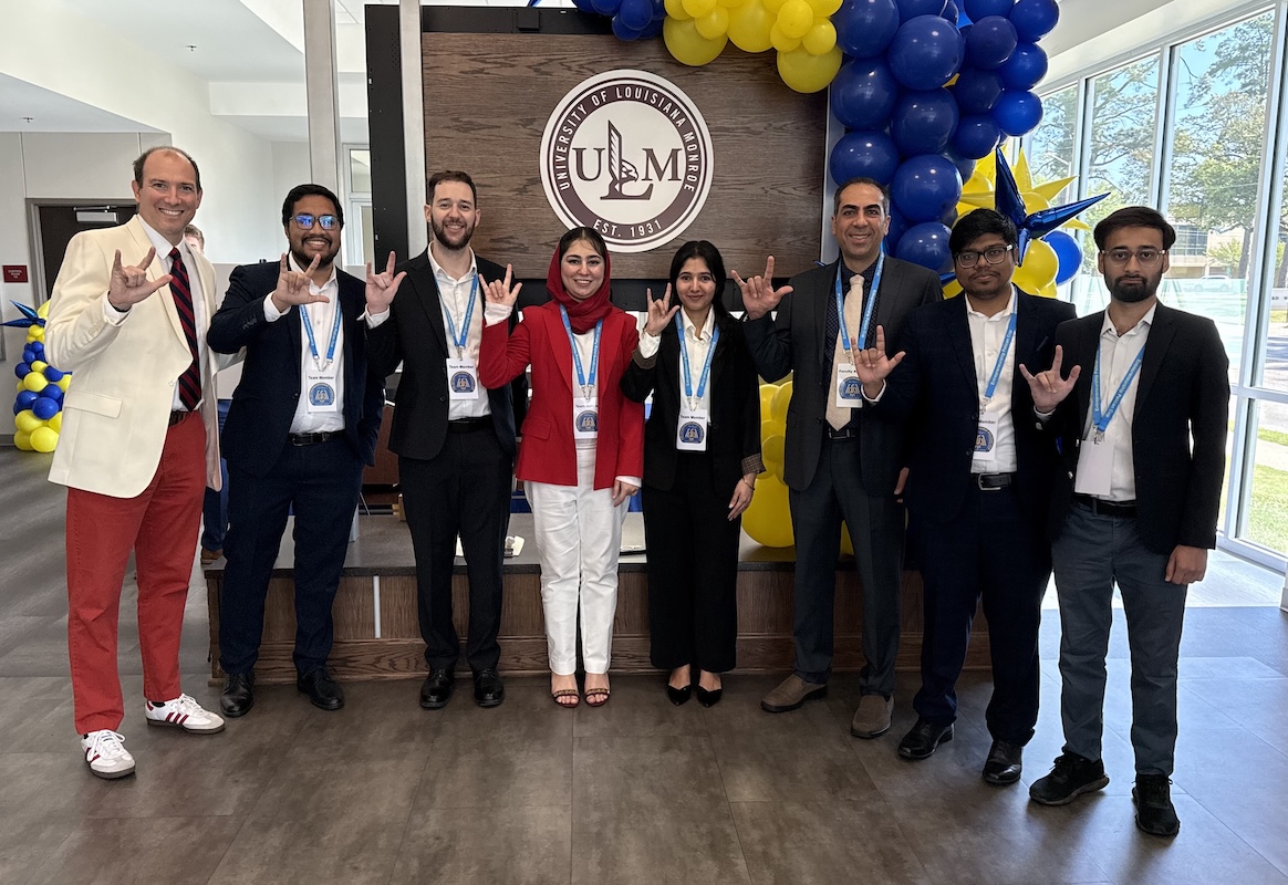 Eight people stand in front of a ULM sign holding up UL Lafayette hand signs.