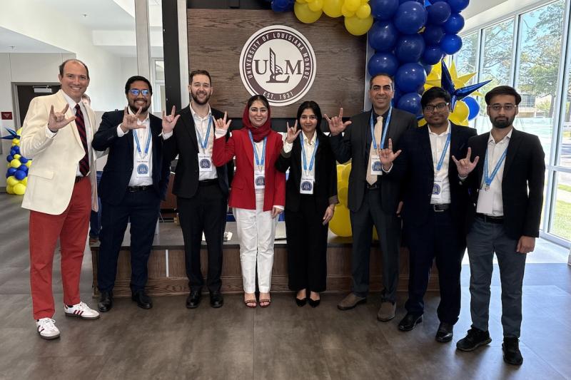 Eight people stand in front of a ULM sign holding up UL Lafayette hand signs.
