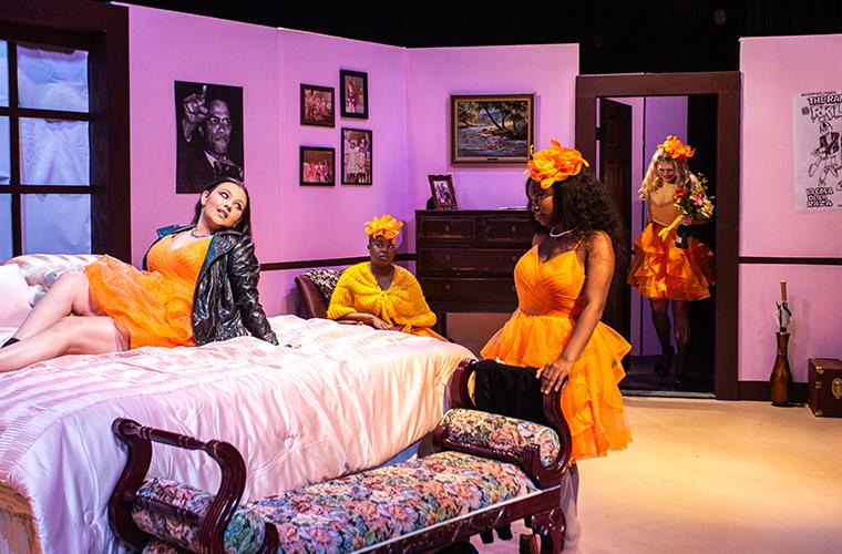 UL students appear in a bedroom on stage wearing similar orange dresses