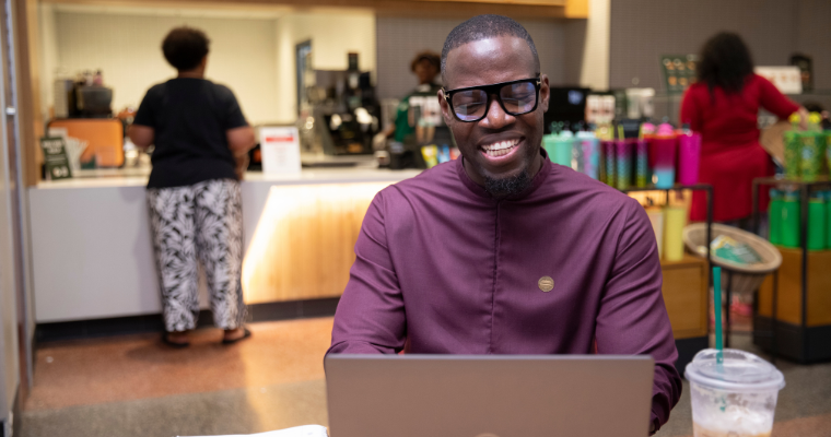 Student in an online accelerated degree program smiles while completing coursework on his laptop.