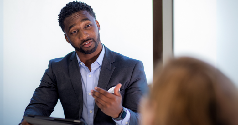 Online finance MBA grad presents in a conference room wearing formal work attire
