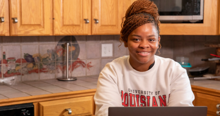 Graduate of UL Lafayette's online health services admin program smiles while working on laptop. 