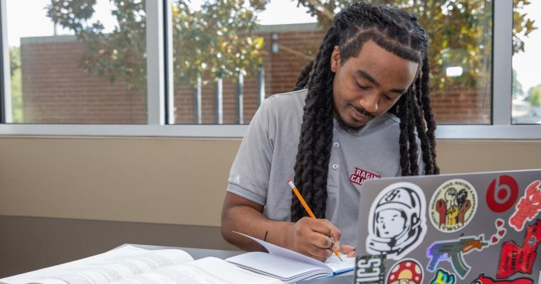 Online student studies at laptop, wearing a gray Ragin' Cajun t-shirt.