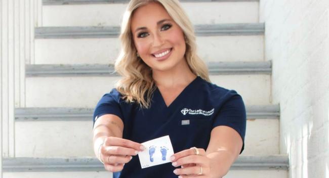 Graduate of UL Lafayette's online RN to BSN sits on a staircase wearing scrubs, holding a NICU emblem.